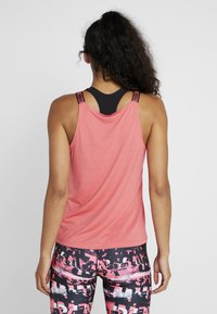 Czarny sportowy biustonosz z wyściółką pod luźnym różowym topem o fakturowanym wykończeniu; w zestawie z legginsami w różowo-czarny wzór.