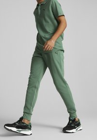 Grön atletisk outfit bestående av en polotröja och matchande byxor. Tröjan har en krage och en ficka; byxorna har sidodetaljer. Svarta och gröna skor fulländar looken.