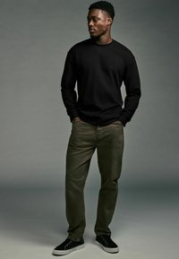Schwarzes Langarmshirt, olivgrüne Hose, schwarze Sneaker mit weißen Sohlen. Einfaches Design, lässige Passform und keine sichtbaren Muster oder Logos.