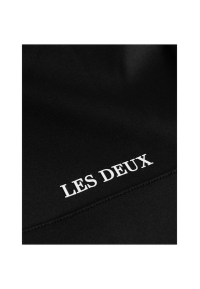 Черен плат с текста "LES DEUX" в бяло, видими шевни линии и гладка текстура, която показва, че е предназначен за облекло.