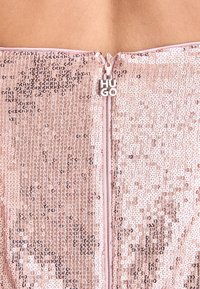 Gros plan d’un tissu rose à sequins avec une fermeture éclair centrale arborant des lettres argentées formant le mot HUGO sur le curseur.