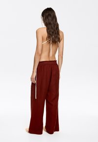 Back view of a person wearing brown linen wide-leg pants with an elastic waist and tied straps, featuring a smooth, textured fabric.
