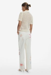 Háčkovaný svetlý žltý top s krátkym rukávom skombinovaný s širokými bielymi nohavicami s farebnou výšivkou mušlí a hviezdic. Hladká textúra a pohodlný strih.