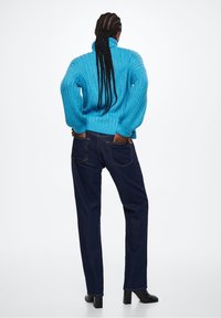 Blue ribbed knit sweater with a high collar, paired with dark blue straight-leg jeans. Model wears black ankle boots.