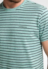 Lichtgroen T-shirt met korte mouwen, voorzien van horizontale zwarte strepen en een klein logo met de tekst "PETROL INDUSTRIES" in zwart.