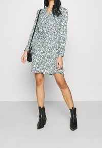 Blommig klänning med v-ringning, långa ärmar och en figursydd midja. Svarta ankle boots fulländar outfiten, med spetsig tå och klack.