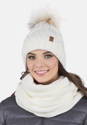 Bonnet en tricot blanc avec un pompon en fourrure et une écharpe infinie assortie, présentant un motif texturé et un accent en cuir avec logo.