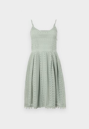 Jasnozielona sukienka z koronką, z cienkimi ramiączkami, dopasowanym gorsetem i rozkloszowaną spódnicą z misternymi wzorami wyciętymi i falbaniastym dołem.