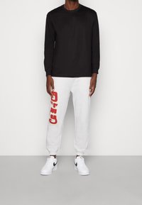 Svart långärmad skjorta i kombination med grå sweatpants med röda "CATO"-bokstäver. Vita sportskor med svarta detaljer.