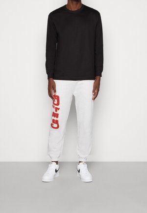 Langærmet sort skjorte kombineret med grå sweatpants med rød "CATO" tekst. Hvide sportsko med sorte accenter.