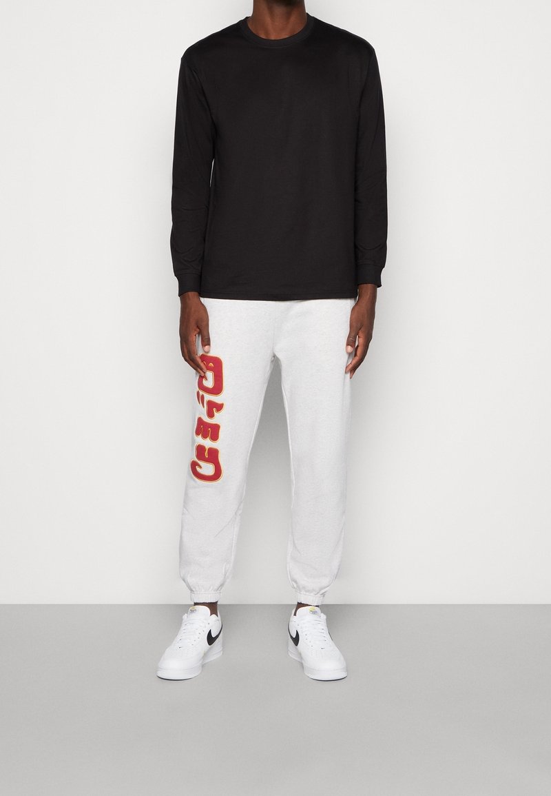 Svart långärmad skjorta i kombination med grå sweatpants med röda "CATO"-bokstäver. Vita sportskor med svarta detaljer.