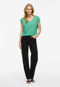 Top verde de manga corta con escote en V combinado con pantalones negros de corte relajado, que presentan una textura suave y un diseño clásico. Sandalias negras de punta abierta.