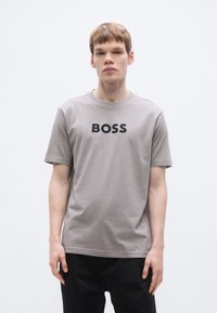 Γκρι βαμβακερό t-shirt με κοντά μανίκια, διαθέτει τολμηρό μαύρο λογότυπο "BOSS" στο μπροστινό μέρος, στρογγυλή λαιμόκοψη και άνετη εφαρμογή.