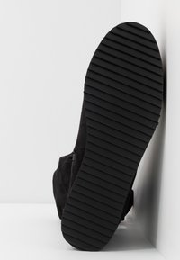 Czarny zamszowy but widziany od dołu, wyposażony w żłobioną gumową podeszwę o płaskim profilu i minimalnym zdobieniu.