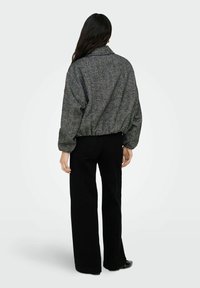 Veste surdimensionnée texturée noire et grise avec col, taille élastique et manches longues, associée à un pantalon noir à jambes larges.