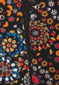 Tissu à motifs avec des motifs floraux et de papillons vibrants en bleu, rouge et orange sur un fond noir, avec un détail de bordure découpée.