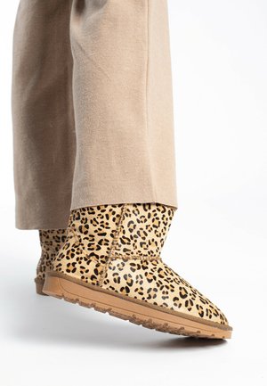 Beige nahkaleopardimustriga ankle boots tekstuuriga pinnaga ja kummitald, kombineeritud beige lõdva istumisega pükstega.