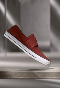 Piros velúr, slip-on cipő, kiemelkedő fehér gumitalppal, textúrával ellátott orral és visszafogott vízszintes varrásokkal.