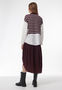 Pull cropped rayé maroon et blanc porté sur une chemise blanche, associé à une jupe fluide maroon et des bottes noires jusqu'aux genoux.