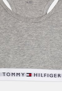 Top de algodón gris sin mangas con tirantes anchos, que presenta una banda elástica blanca con el texto y el logo de "TOMMY HILFIGER" en rojo y negro.