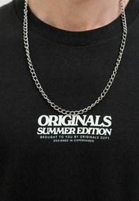 Must värvi puuvillane T-särk, millel on valge tekst "ORIGINALS SUMMER EDITION" ja hõbedane kett, mis on kaela ümber riputatud.