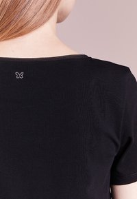 Black ribbed t-shirt with short sleeves, featuring a circular neckline and a small butterfly design in rhinestones on the back.
