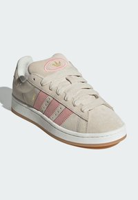 Beige suede sneaker with pink three stripes and logo patch. Textured material, flat white midsole, and gum rubber outsole.