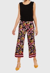 Haut sans manches noir associé à un pantalon large avec un motif floral vibrant en jaune, rose et vert, avec des accents rouges rayés.