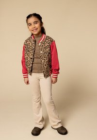 Luipaardprint varsityjack met rode mouwen, beige geribbelde coltrui, crèmekleurige corduroy broek en bruine instappers.