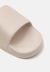 Beige Riemensandalette mit einem breiten, strukturierten Obermaterial und einem glatten, konturierten Fußbett. Die Sohle hat eine leichte Plattform mit abgerundeten Kanten.