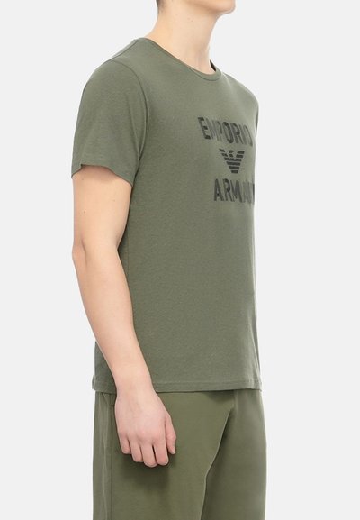 T-shirt vert olive en tissu doux, avec un col rond et des manches courtes, orné d'un logo noir "Emporio Armani" imprimé sur le devant.