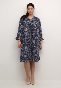 Vestido de manga larga en una tela azul marino con un estampado de paisley, con escote en V y mangas acampanadas, que llega por debajo de la rodilla.