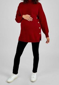 Vestido suéter rojo de punto con cuello alto, botones laterales y ajuste holgado, combinado con leggings negros y zapatillas blancas.