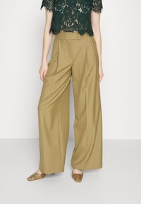 Wijdzijdige chino's van kaki stof met een getailleerde pasvorm, voorzien van voorplooien en een enkele knoopsluiting. G gedragen met een donkere kanten crop top.