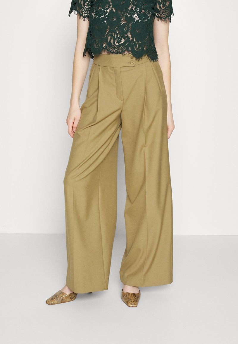 Wijdzijdige chino's van kaki stof met een getailleerde pasvorm, voorzien van voorplooien en een enkele knoopsluiting. G gedragen met een donkere kanten crop top.