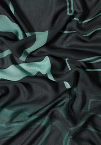 Zwarte stof met een gladde textuur, versierd met teal geometrische patronen in verschillende vormen, die een gelaagde, vloeiende uitstraling creëren.