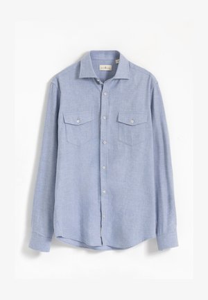 Camisa de manga larga azul claro hecha de tela texturizada. Cuenta con cierre de botones al frente, dos bolsillos en el pecho con solapa y dobladillo redondeado.