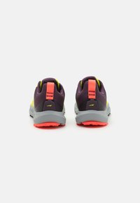 Zapatillas deportivas moradas y amarillas con una parte superior texturizada, entreplantas grises y llamativos acentos rosas en el talón y la suela.