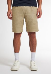 Beige Leinen-Shorts mit einem lässigen Schnitt, Midi-Länge und einem elastischen Bund. Kombiniert mit weißen Sneakers und gerippten weißen Socken.