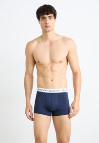 Boxeri din bumbac bleumarin, cu un elastic alb pe care este inscripționat numele brandului în repetate rânduri. Textură netedă și design ajustat.