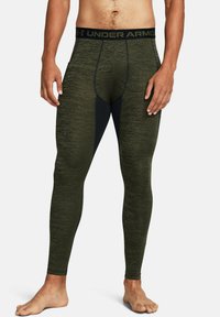 Green fitted leggings made of textured material with a black Under Armour waistband and seam detailing, featuring a snug, athletic design.