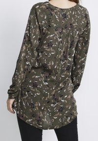 Langourige blouse met lange mouwen in olijfgroen met een bloemenpatroon. Heeft een ronde halslijn, losse fit en een gebogen zoom. Zachte stoftextuur.