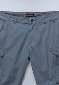 Pantalones cargo grises de corte relajado, confeccionados en material ligero. Incluyen cierre de botón, bolsillos y una pequeña insignia de bandera.