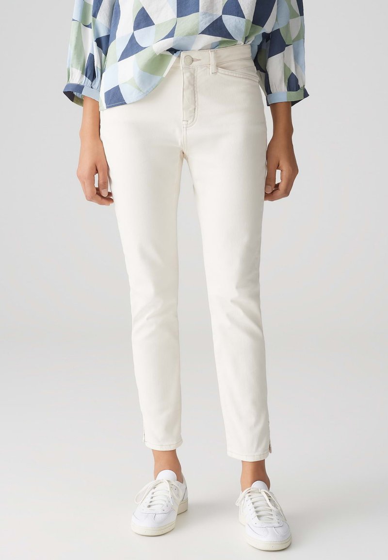 White skinny jeans with a classic five-pocket design and subtle stitching details, paired with white sneakers.