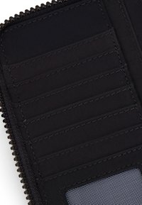 Interno di un portafoglio zip nera con più scomparti per carte, tessuto liscio e una finestra trasparente per l'identificazione. Dettagli di cucitura ordinati.