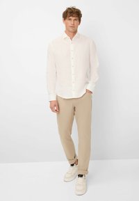 Witte linnen blouse met knoopsluiting, opgerolde lange mouwen, beige slim-fit broek en witte sneakers met zwarte accenten.