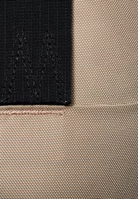 Svart tygpanel med strukturerad söm, intill en beige, slät textilyta. Synlig söm med ljus tråddekoration.