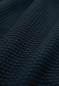 Tmavě modrá texturovaná tkanina s mřížkovým vzorem, která má vyvýšený povrch a přidává hloubku a rozměr materiálu.