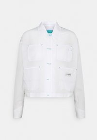 Giacca bianca corta con cuciture blu, chiusura con bottoni, quattro tasche frontali e una piccola toppa con il logo Converse sulla tasca inferiore destra.