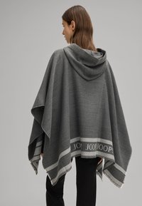 Poncho grigio con cappuccio, realizzato in morbido tessuto. Presenta una striscia bianca a contrasto con il nome del marchio. I bordi sono frangiati.